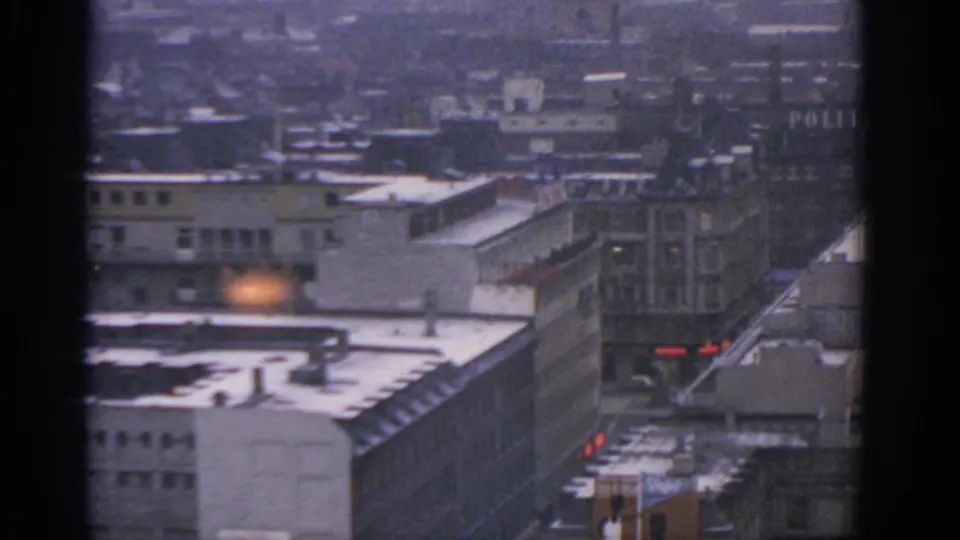 1963 Warsaw rooftops and street edge in haze, with partial POLITIKEN lettering at right and small red lights near the lower frame.