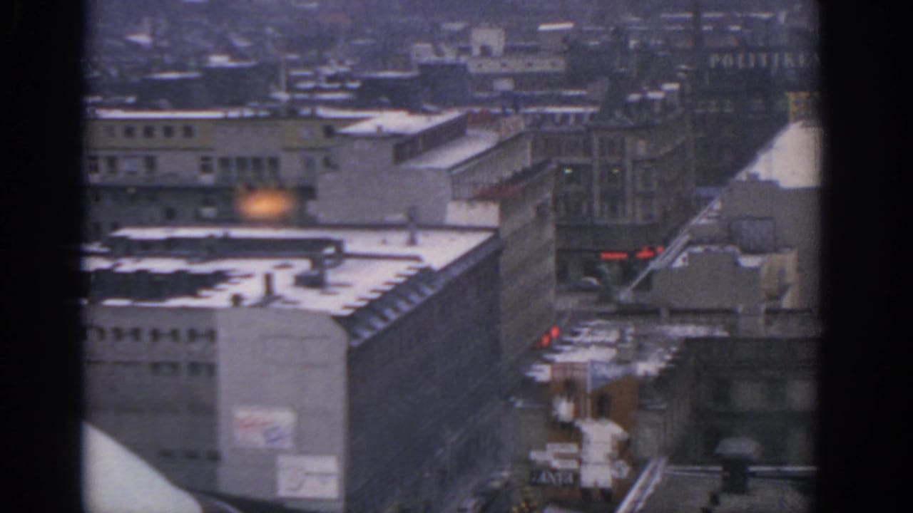 1963 Warsaw high-angle view with snowy rooftops, large urban buildings, signage, and a street receding between blocks.