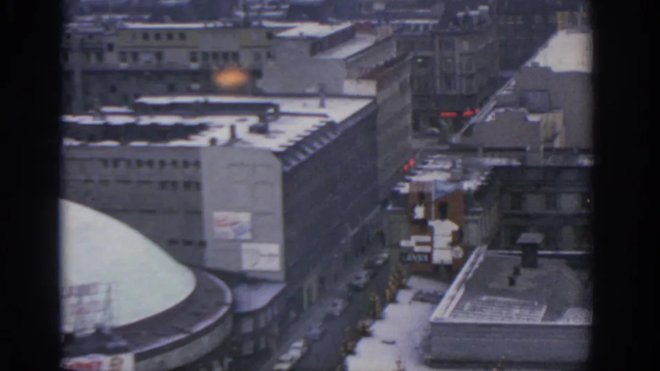1963 Warsaw view showing a curved or domed roof, snow-covered streets, parked cars, tall buildings, and a small orange glow in the distance.