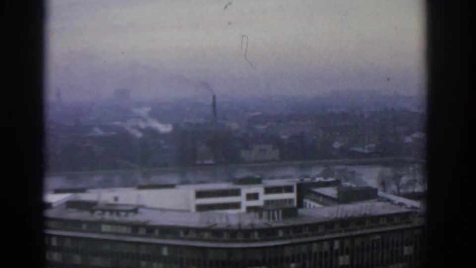 1963 Warsaw skyline under grey haze, showing a river, distant smokestacks, low buildings, and a large foreground roofline.