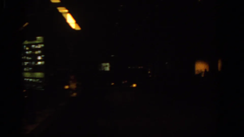 Dark 1963 travel footage frame, likely inside a vehicle or room, with streaked ceiling lights and distant illuminated rectangles.