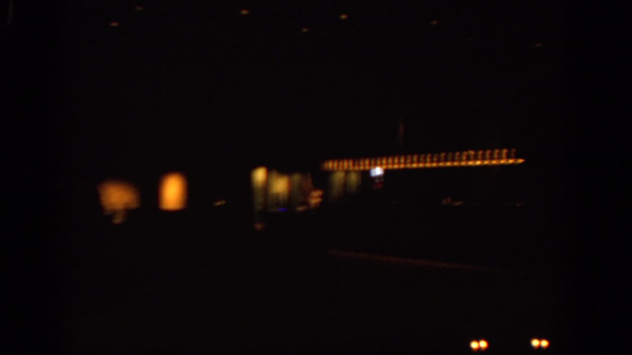 1963 Warsaw night footage showing warm illuminated windows or signage against a very dark street scene from a moving viewpoint.