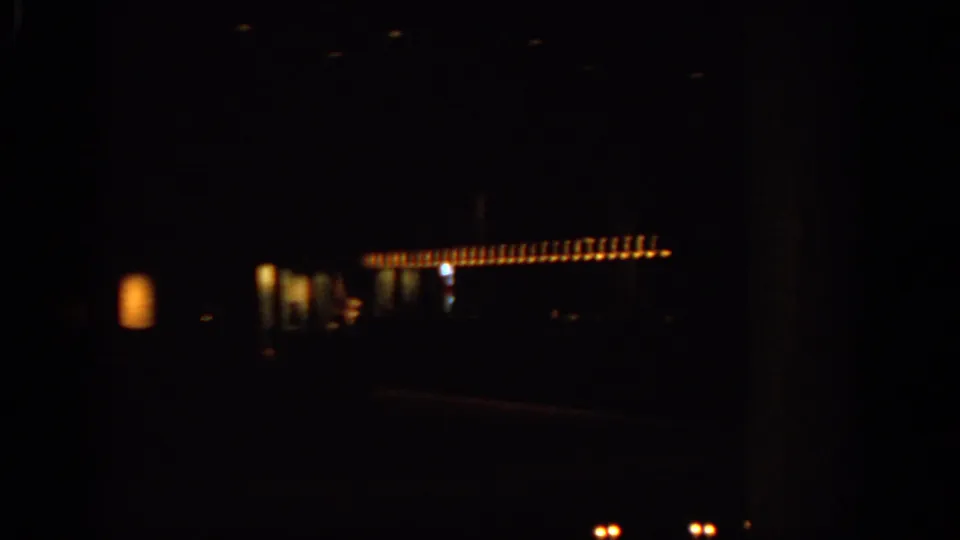 A moving 8mm night view in Warsaw shows a horizontal row of warm lights with surrounding buildings mostly lost in shadow.