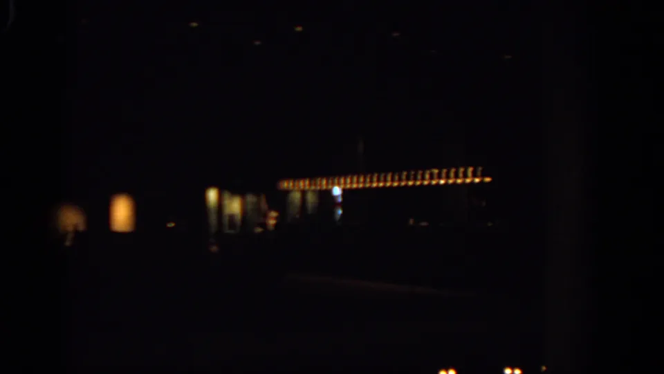 Underexposed 1963 Warsaw night footage shows warm illuminated building details and faint street forms from a moving camera.