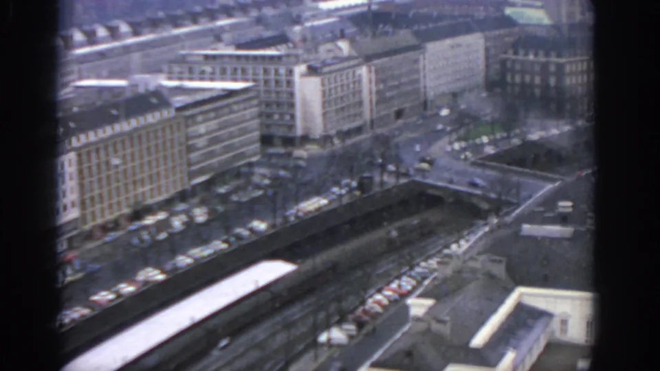 1963 Warsaw window view over a busy street, rooftops, and mid-century urban buildings seen through dark frame edges.