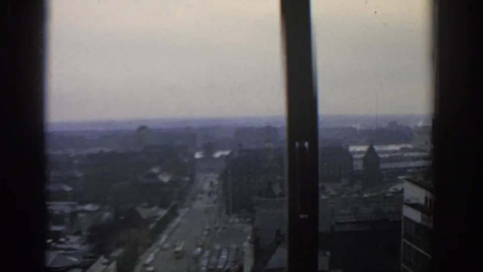 1963 Warsaw street traffic seen from a high interior vantage point through vertical window frames.
