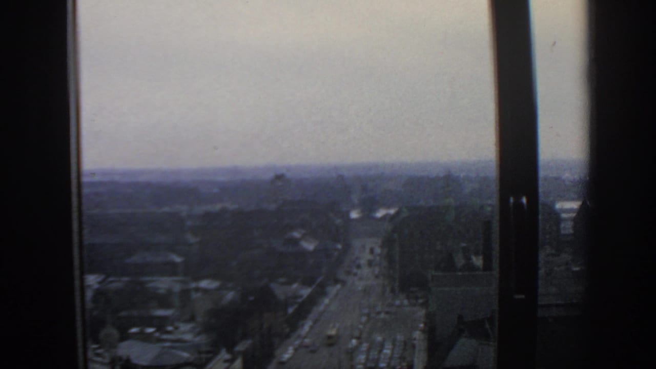 City roadway and traffic viewed through a tall window frame.