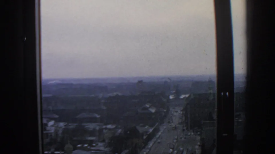 A high, grainy 8mm view over Warsaw traffic, with dark window mullions dividing the frame.