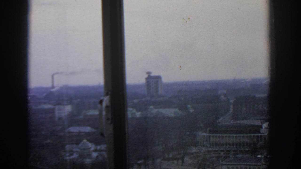 Overcast city view through dark window frames with distant buildings and smoke.