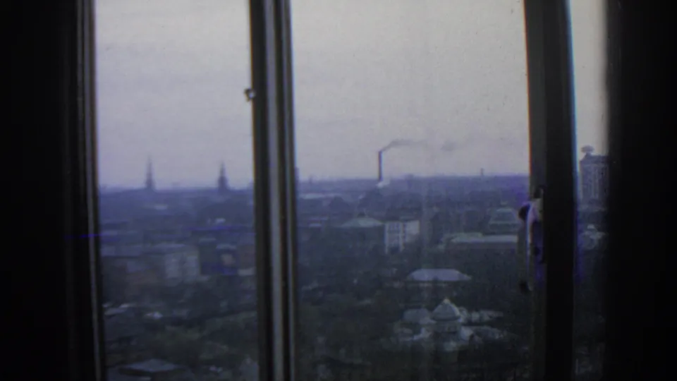 The final frame holds a muted 1963 Warsaw skyline through a window, with distant industrial smoke, rooflines, trees, and visible window hardware.