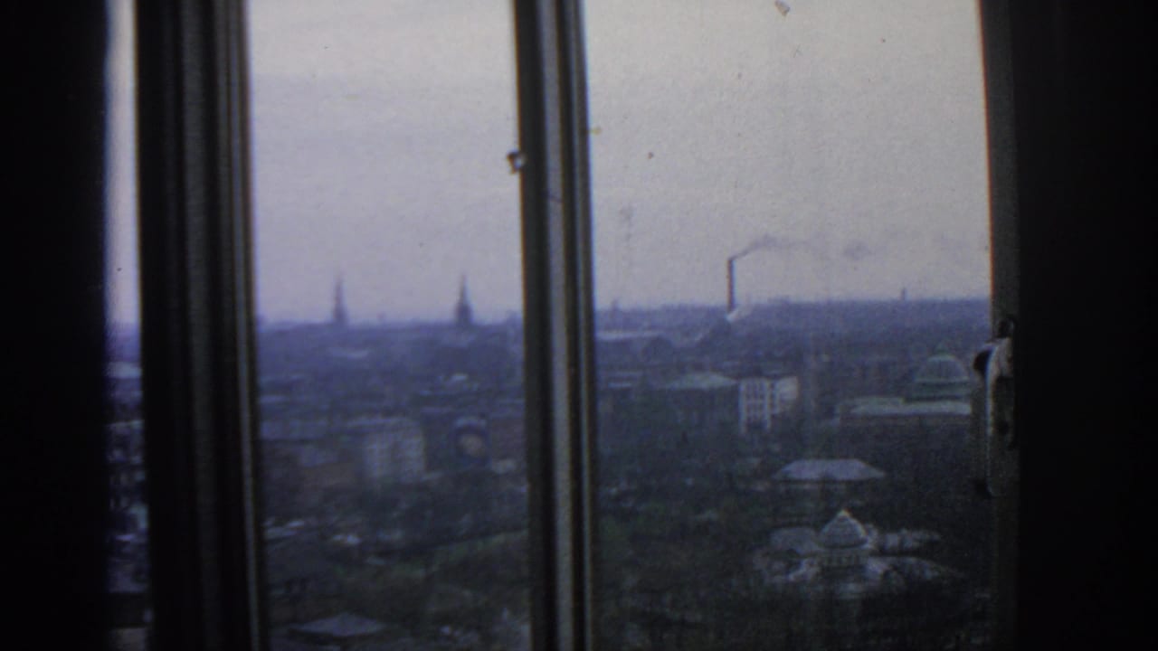 1963 Warsaw skyline viewed through interior window frames, with distant rooftops, spires, and a smoking chimney.