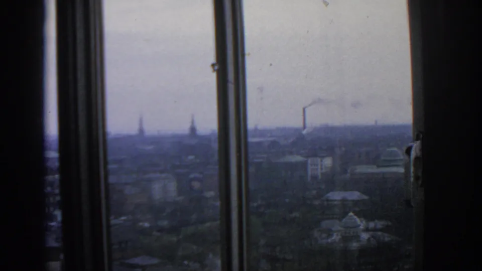 1963 Warsaw skyline viewed through interior window frames, with distant rooftops, spires, and a smoking chimney.