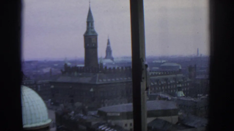 1963 Warsaw view from behind a window, showing a towered landmark, rooftops, streets and a hazy city skyline.