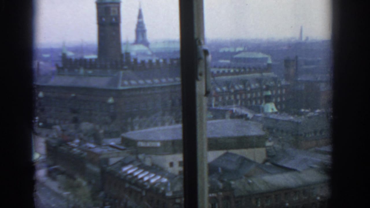 Window-framed elevated cityscape with a towered building, rooftops and streets below.