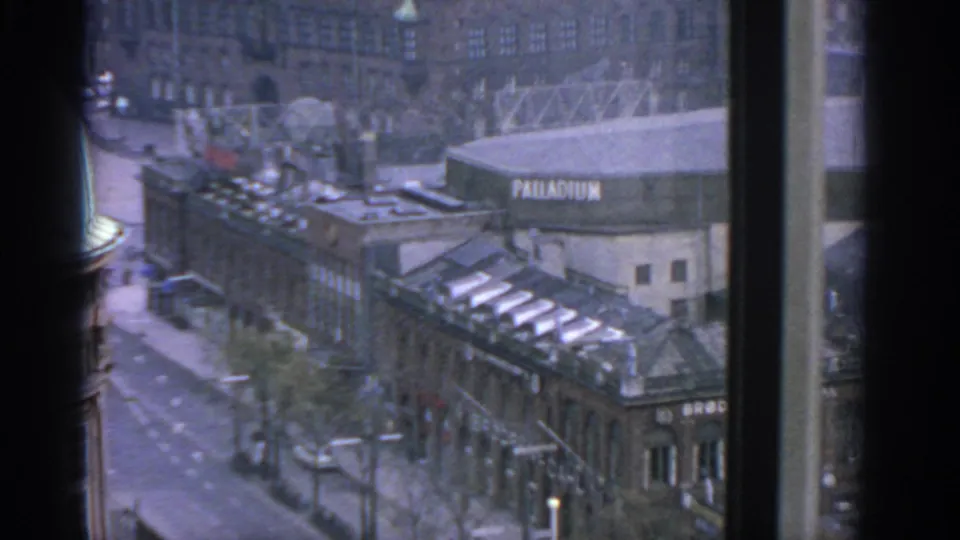 Window-framed 1963 Warsaw view showing the Palladium sign, street traffic, roof structures and surrounding buildings.