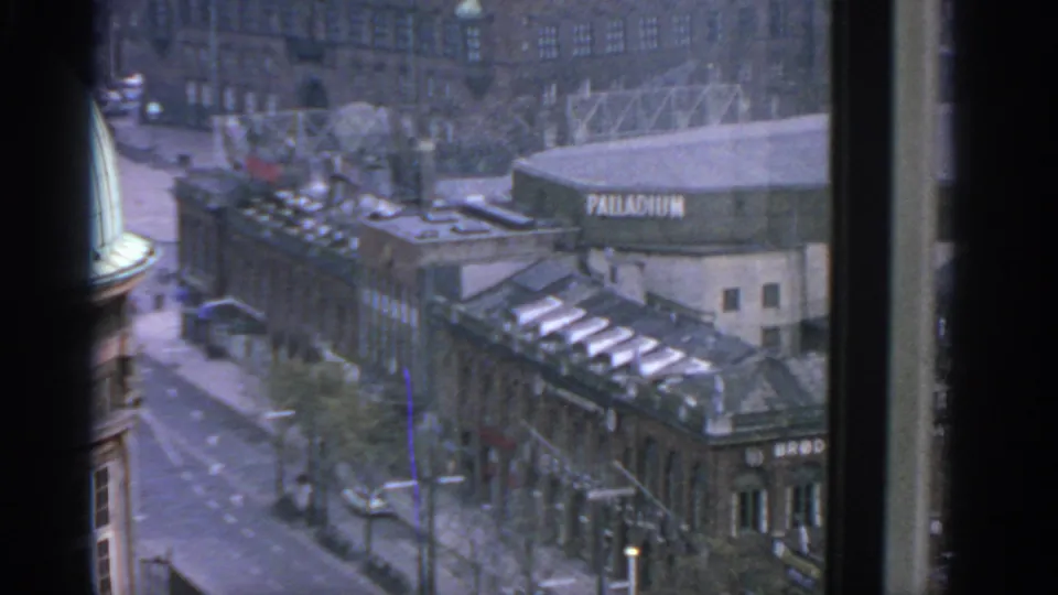 1963 8mm view over Warsaw through dark window framing, showing a street, rooftops, and a prominent PALLADIUM sign.