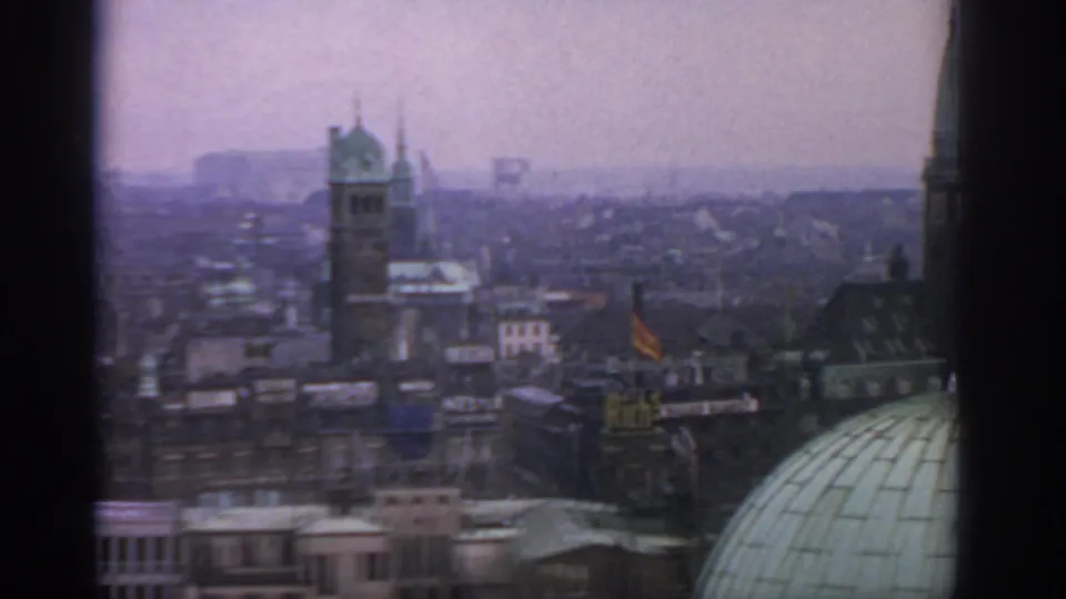 1963 Warsaw city view showing a tower, dense rooftops, small flags, and a green dome under an overcast sky.