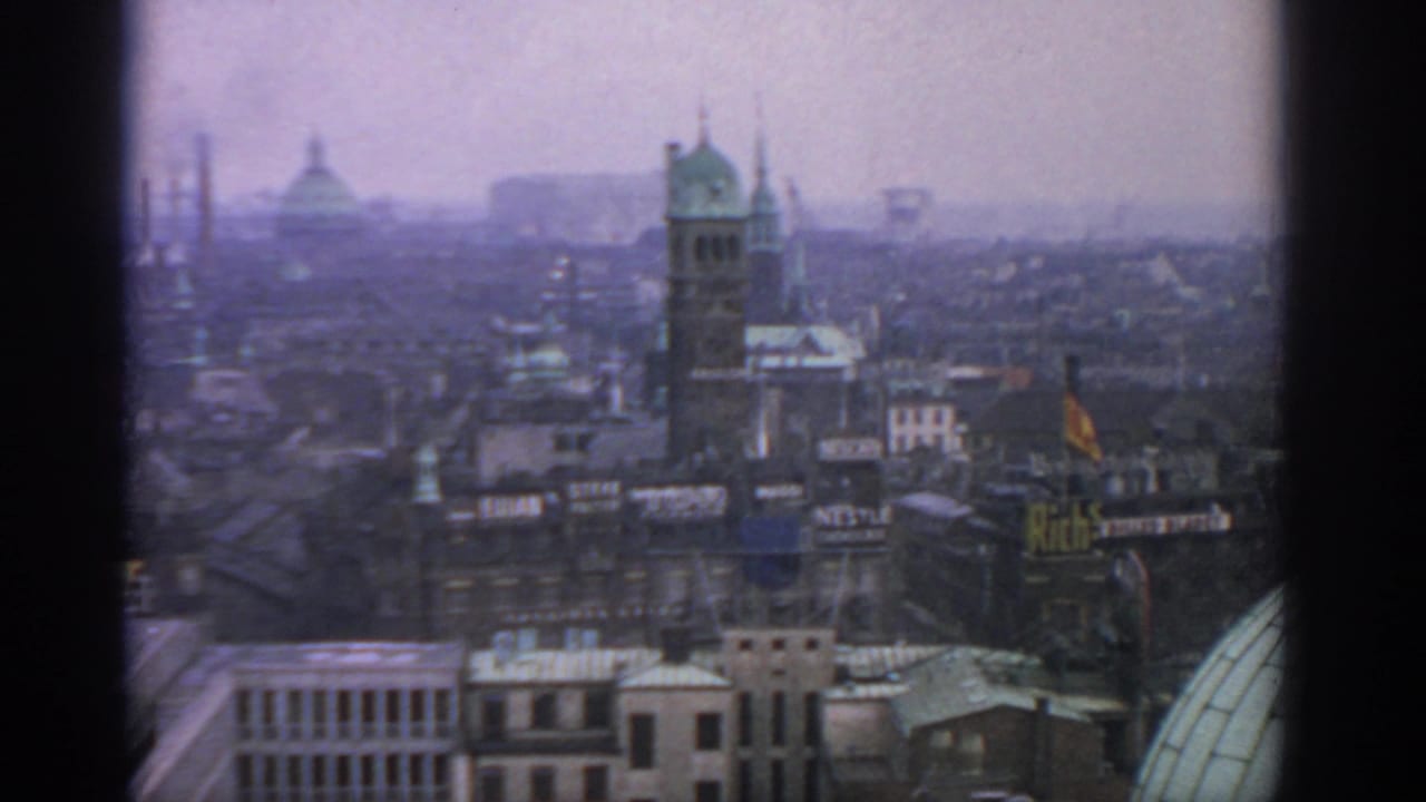 Elevated hazy city skyline with domed roof, spired tower, smokestacks, and rooftop signs.