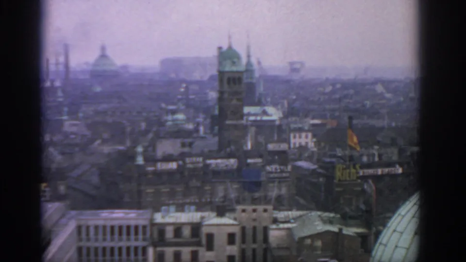 1963 Warsaw city view from above with a green-spired tower, domed roof, industrial smoke, and visible rooftop advertising.