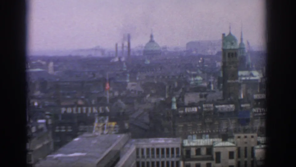 Late frame of the 1963 Warsaw panorama with a prominent rooftop sign, factory stacks, domed roof, tower, and foreground commercial buildings.