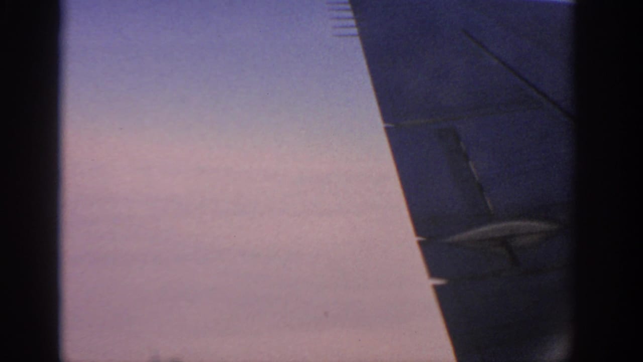 Aircraft wing and dark tail or engine area against a pale pink-blue sky.