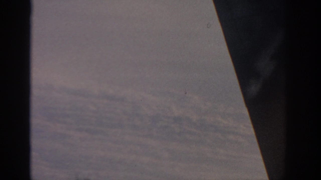 Clouds seen through an airplane window with dark aircraft edges in frame.