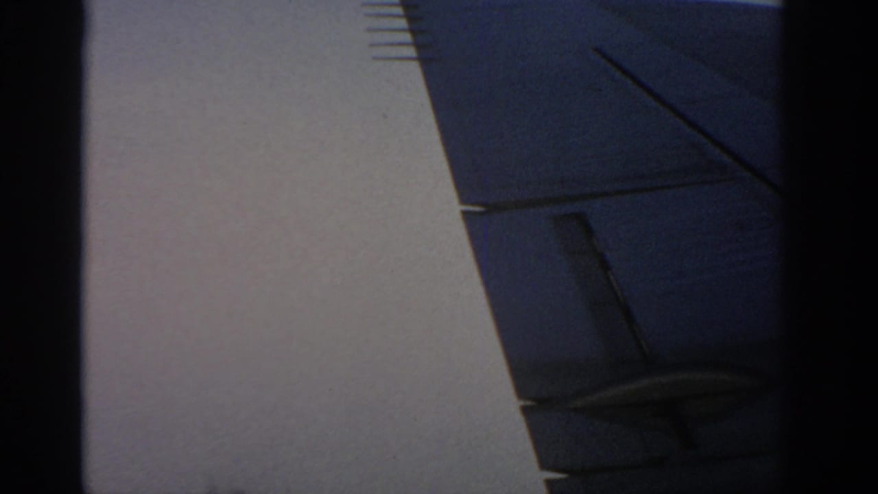 1963 Warsaw home-movie frame showing a light exterior wall and angular blue-gray building detail, with the view partly obscured.