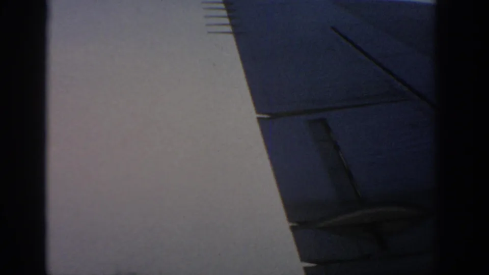 1963 Warsaw home-movie frame showing a light exterior wall and angular blue-gray building detail, with the view partly obscured.