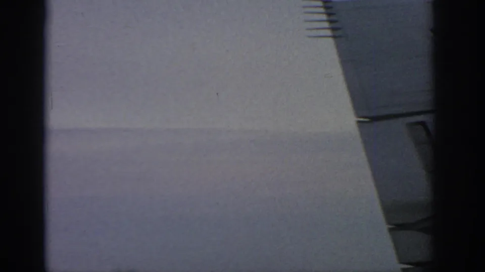 1963 Warsaw 8mm still showing a pale wall area, partial blue-gray facade detail, and a dark vertical border in the foreground.