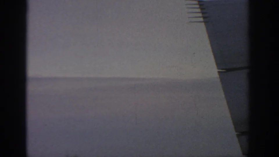 1963 Warsaw home-movie still of a minimal exterior wall and dark angled building element, with grain and muted color visible.