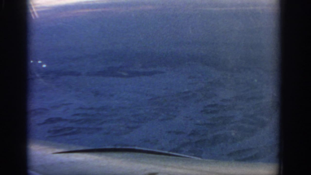 1963 home-movie view over a snow-covered landscape near Warsaw, seen through an airplane window with dark frame edges.