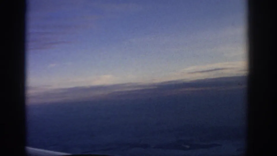 A 1963 airplane-window view over the Warsaw area, showing a dusky horizon and indistinct terrain beneath blue light.
