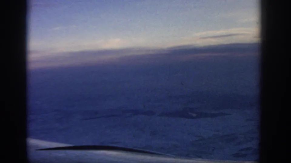 A late-frame 1963 passenger view shows darkened terrain, blue dusk light, and part of the aircraft edge beneath the horizon.