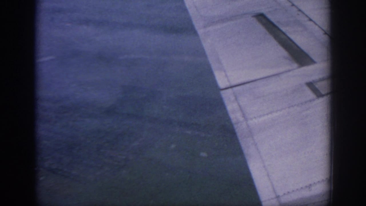 1963 Warsaw travel footage frame showing an airplane wing from a passenger-window viewpoint against dark clouded sky.