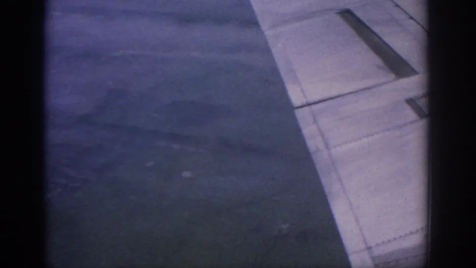 Aircraft wing from a passenger window in low-light 8mm footage associated with a 1963 Warsaw flight.