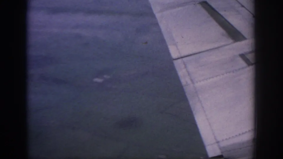 Final 8mm frame of the clip showing the aircraft wing at right and a dim clouded view outside the window.