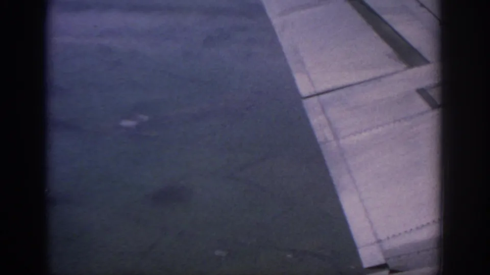 1963 8mm view from an airplane window near Warsaw, showing the wing, flap area, riveted panels, and hazy sky below.