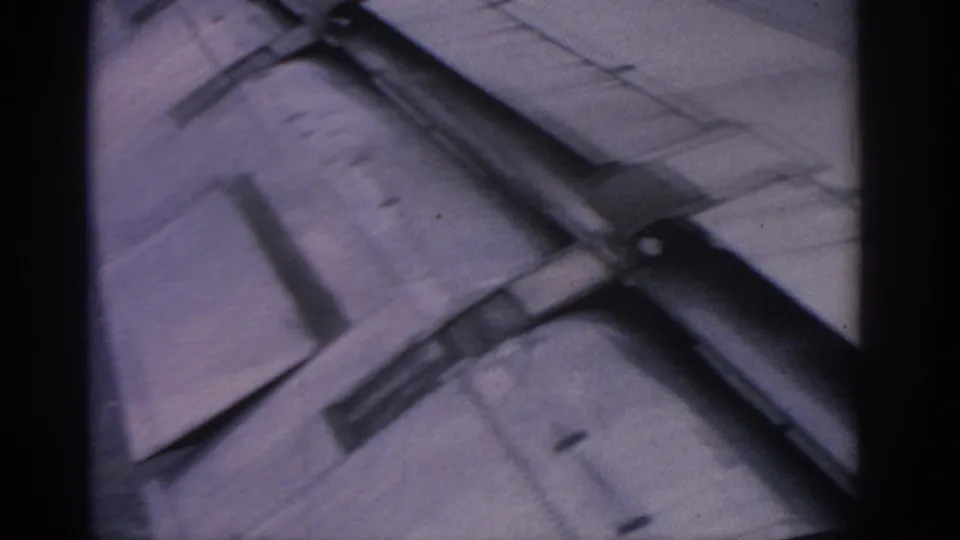 A 1960s 8mm passenger perspective shows the aircraft wing and flap area angled against a muted blue sky.