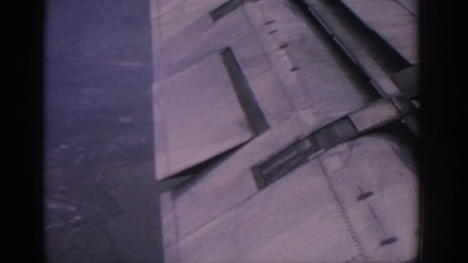 1963 8mm passenger-window view near Warsaw metadata, showing a jet wing, flap surface, and faint ground below.