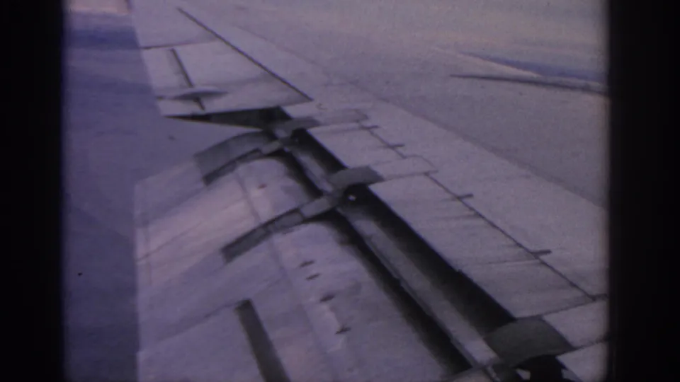 Passenger-window footage from the 1963 Warsaw metadata, with wing structure, flaps, and distant terrain visible.