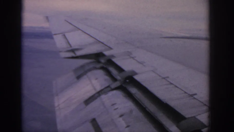 Final 8mm frame shows the jet wing, flap section, and pale sky from a passenger-window perspective.