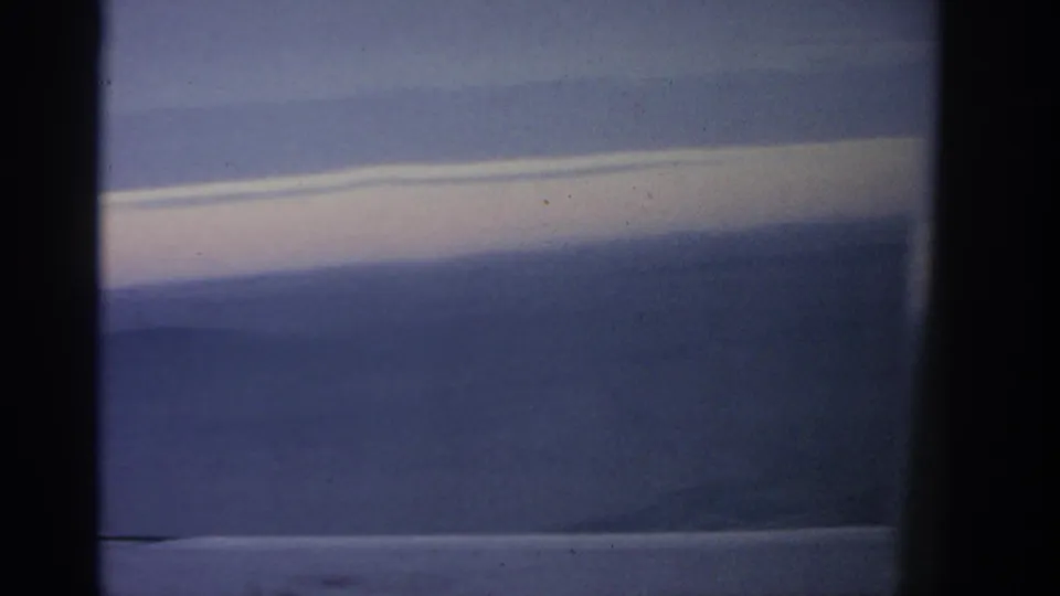 Final 1963 aerial frame near Warsaw, with layered sky, faint ground below, and dark airplane-window dividers in view.