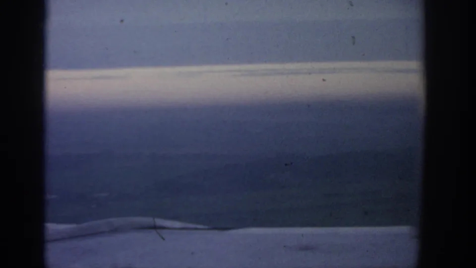 1963 8mm travel frame with a hazy Polish landscape, pale sky band, and a low foreground edge suggesting filming from a vehicle.