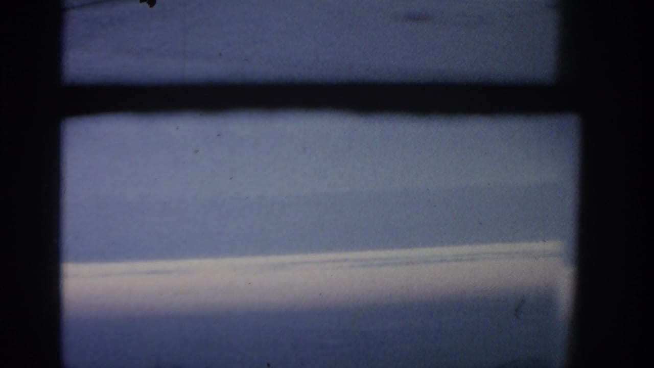 Airplane window frame looking out at blue sky and a pale cloud shelf.