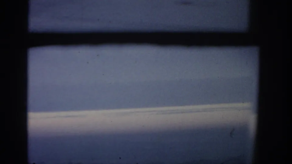 Passenger-window view from 1963 8mm footage, with a dark vertical frame dividing blue sky and a pale cloud band.