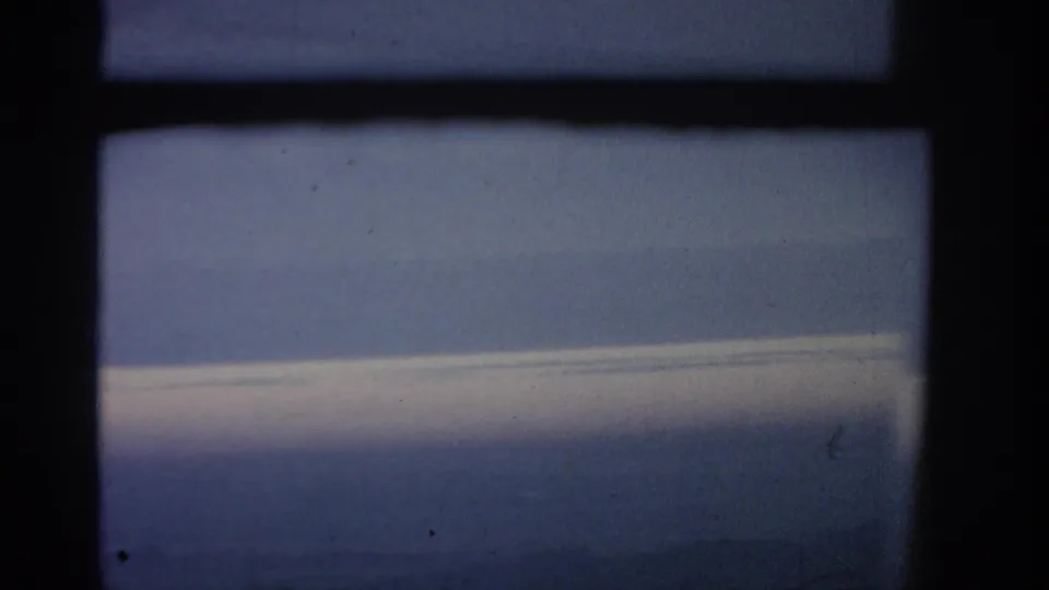 Final 1963 8mm frame of the flight view, showing a blue horizon and pale cloud shelf through dark airplane window framing.