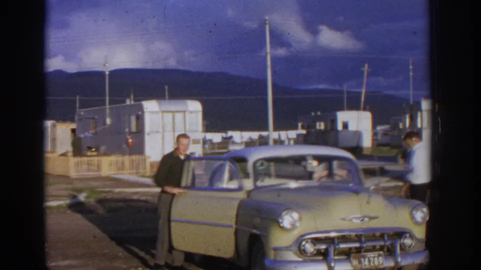 Zurich, Switzerland 1963 frame showing a man opening a pale classic Chevrolet door at a trailer park, with another man partly visible nearby.