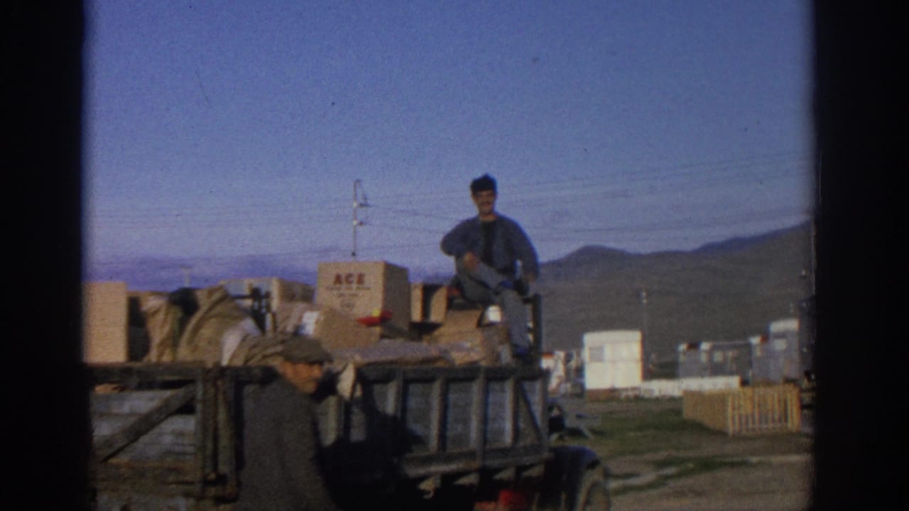 1963 Zurich-area 8mm frame showing men around a truck loaded with crates and an ACE-marked box in a rural mountain setting.