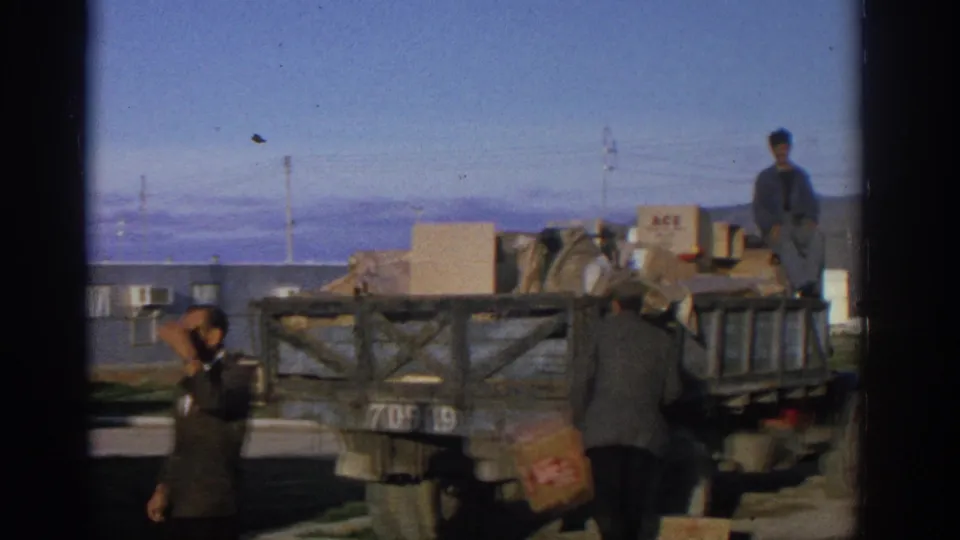 1963 Zurich home-movie frame showing men beside a wooden flatbed truck piled with boxes and bundled goods.