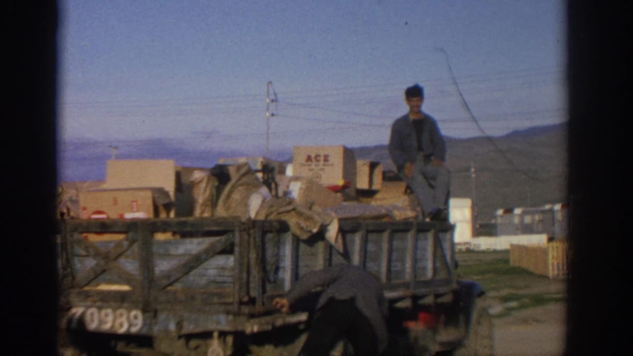 1963 Zurich frame with a man leaning into a loaded wooden truck and another man seated above boxes and covered cargo.